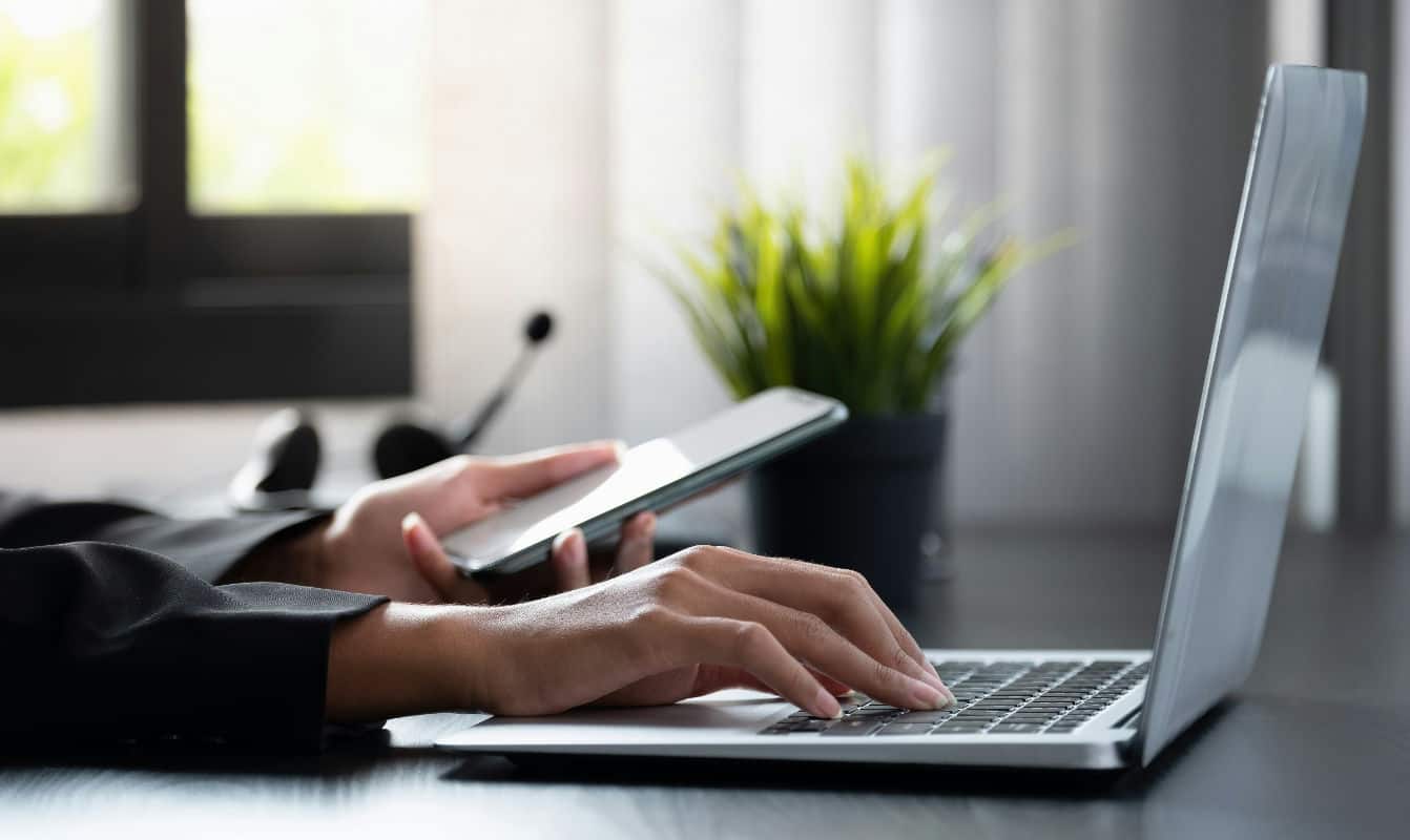 Person using a laptop and smartphone in an office setting.