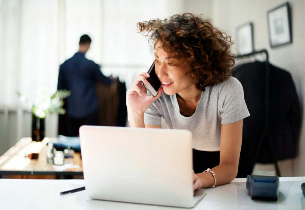 Happy woman talking on phone at work with laptop in modern office.