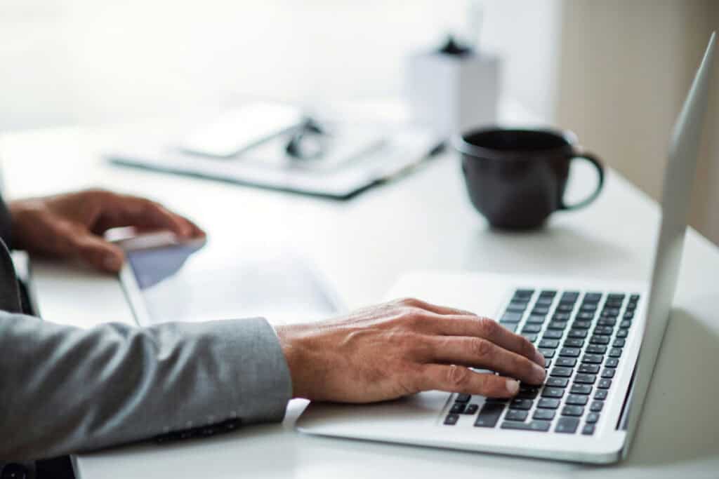 Person working on a laptop at a clean, modern desk with coffee mug and documents.